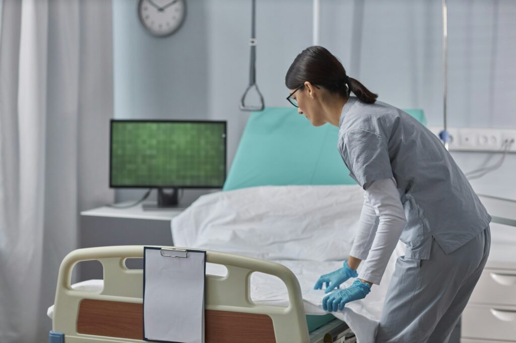 Nurse preparing bed for patient in ward